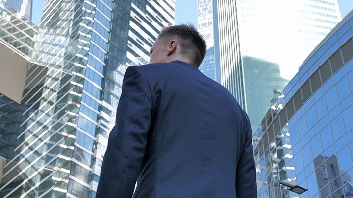 Low-angle view of a person in a suit facing modern skyscrapers.